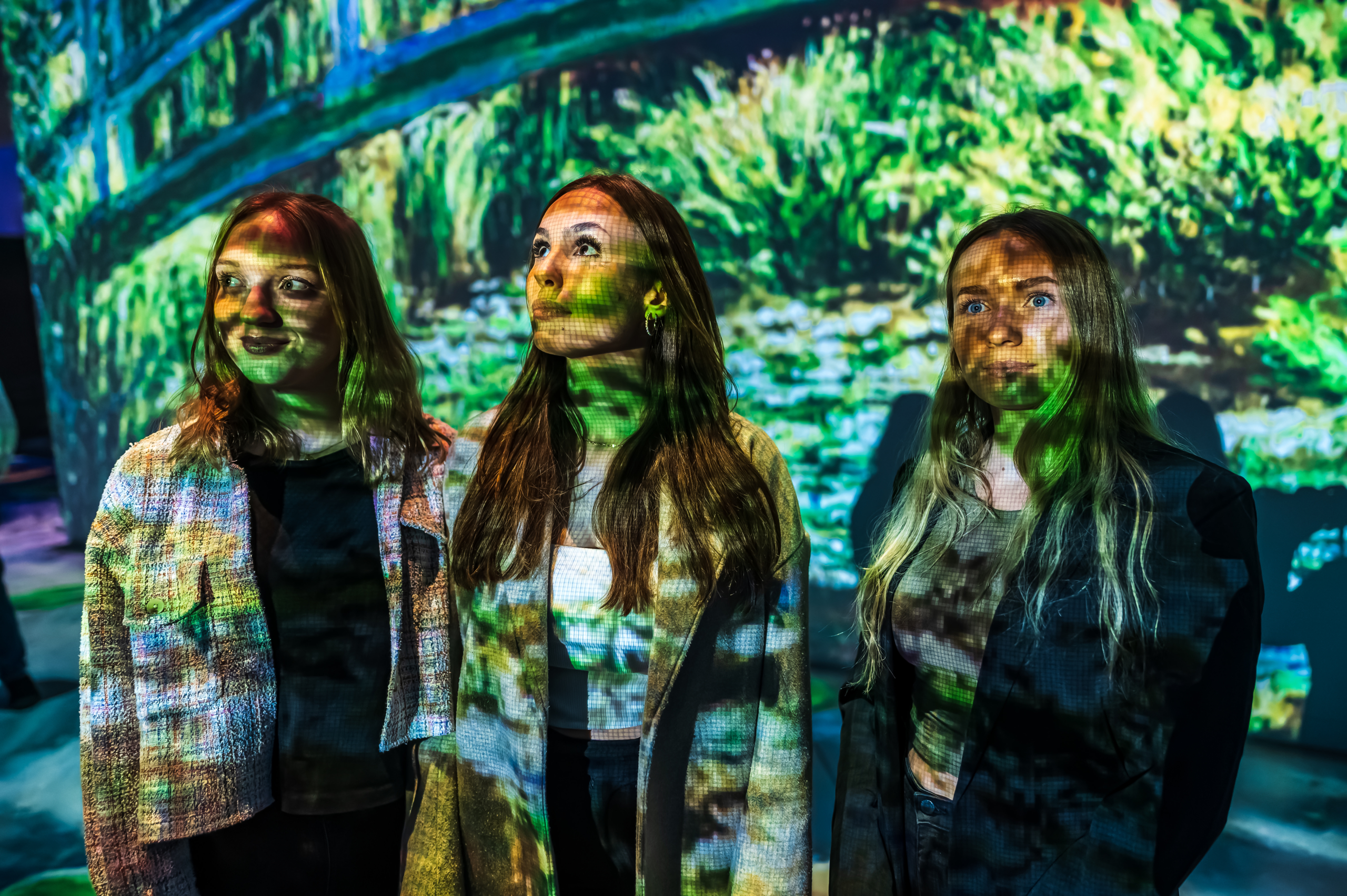 Drei junge Frauen die vor einer Leinwand im Visiodrom stehen. Die Pixel werden auf die Gesichter der Frauen übertragen